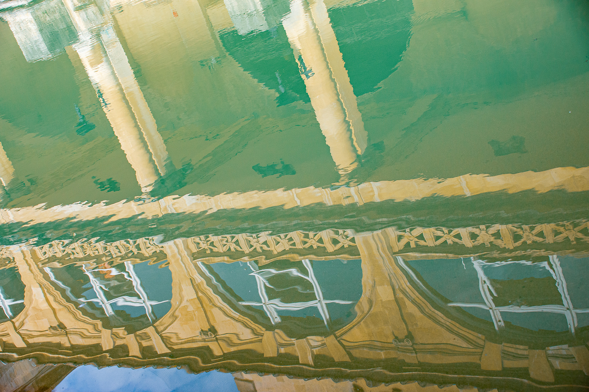The image depicts the ancient Roman Baths in Bath, England. The scene shows a large, rectangular pool of predominantly green and brown, reflections of the building in the pool