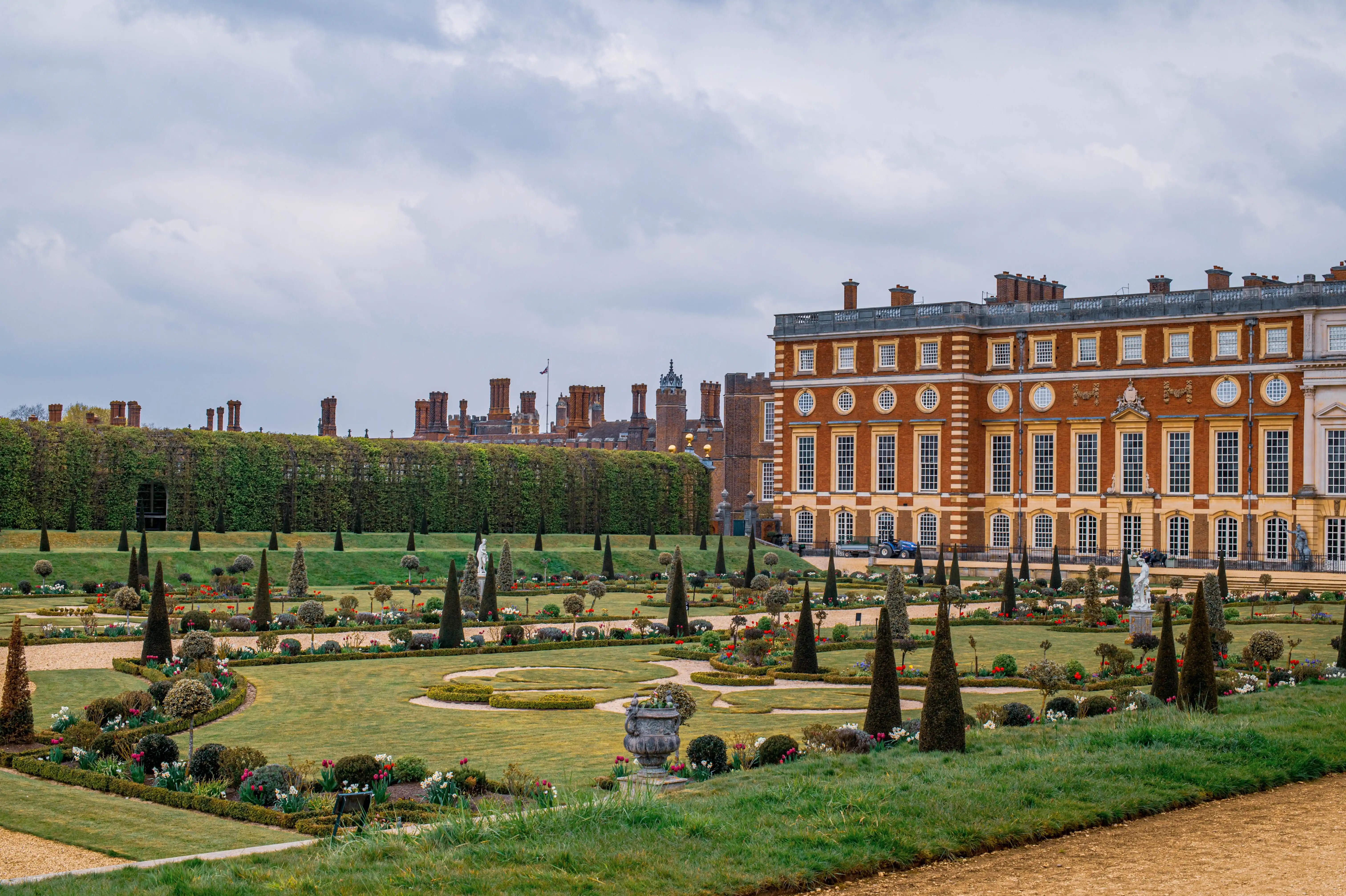 Palace façade with formal geometric garden, topiary trees, statues and manicured hedges.