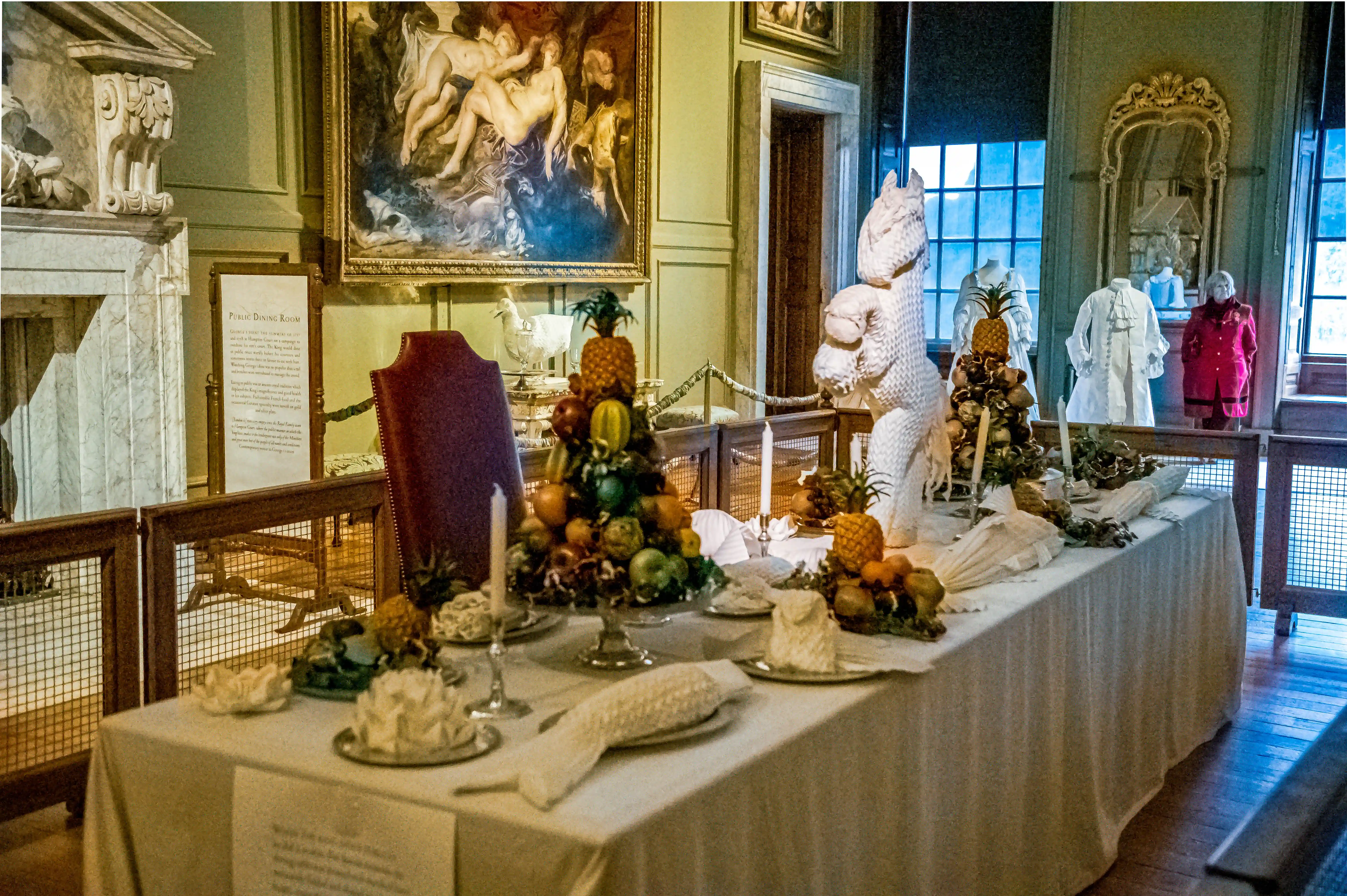 Historic dining room with long banquet table decorated with folded napkins, tall candles and ornate fruit towers.