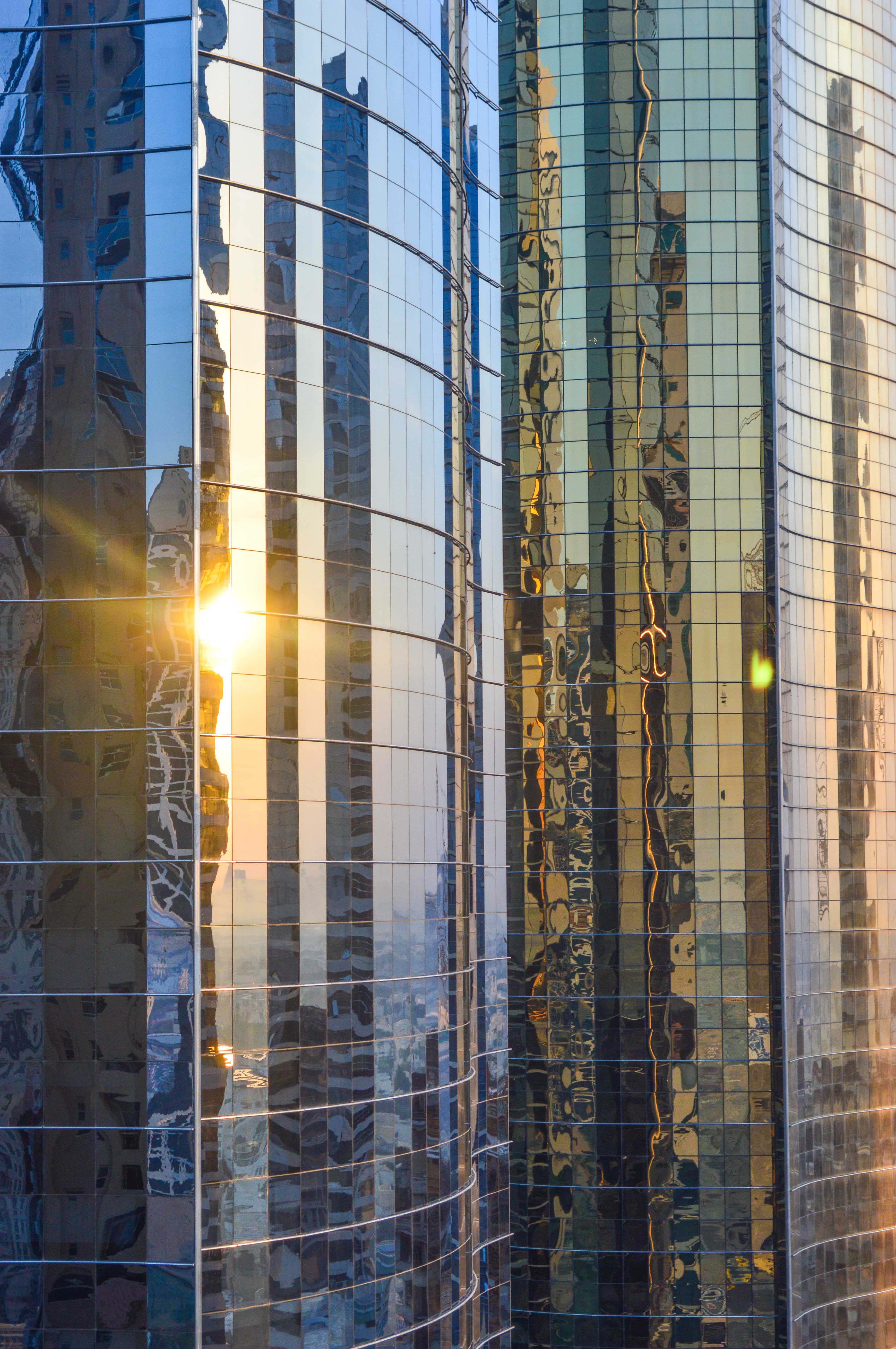 The image showcases a modern building with a reflective glass facade. The sunlight is reflecting off the glass, creating a vibrant and dynamic visual effect. The reflections capture the surrounding environment and the sky, adding depth and complexity to the scene. The building's design emphasizes clean lines and a sleek appearance, highlighting contemporary architectural trends.