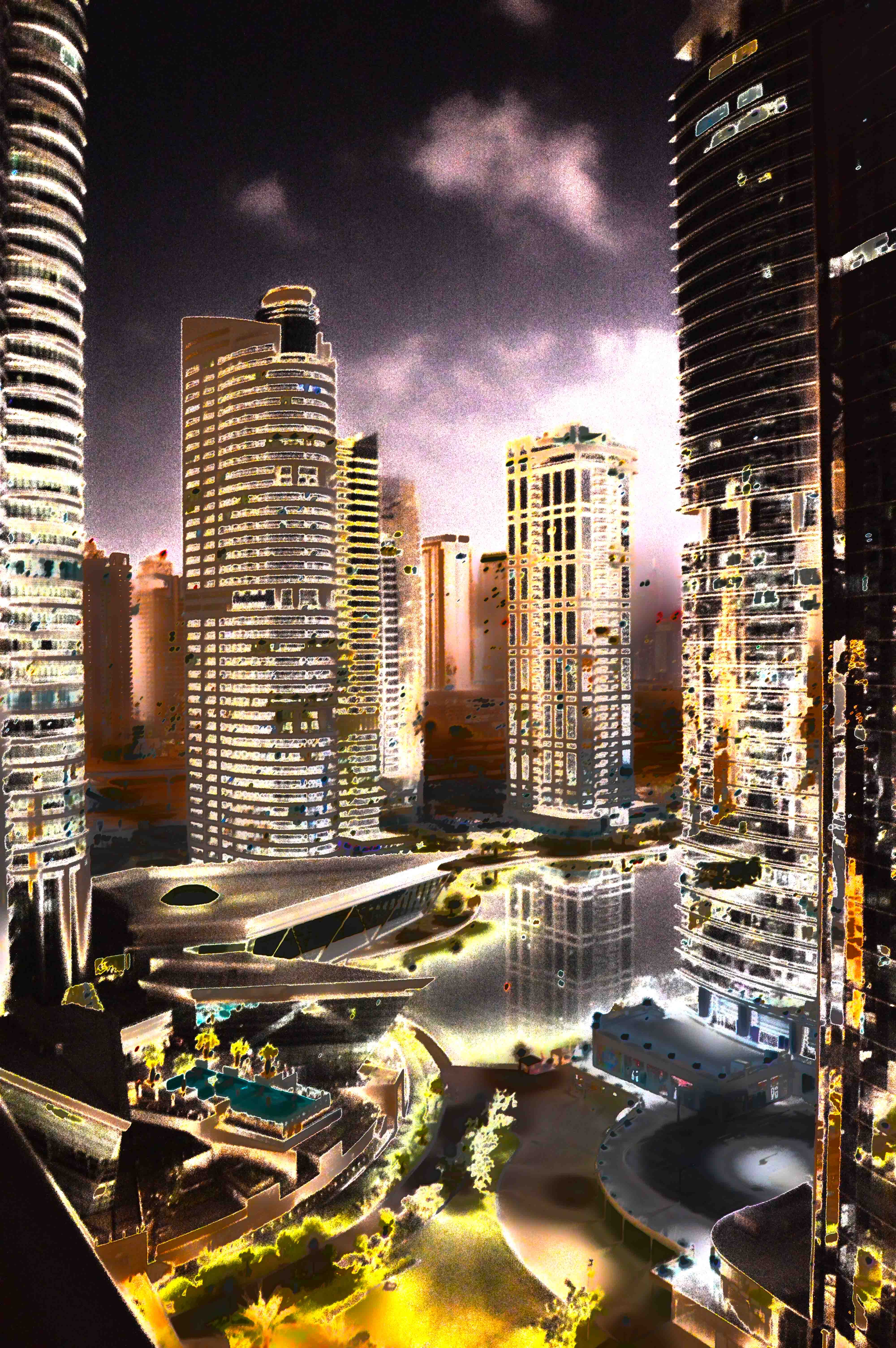 The image depicts a miniature model of a cityscape at night, featuring several tall buildings illuminated with lights. The buildings are detailed with numerous windows and balconies, and the model includes roads, green spaces, and water bodies. The overall scene is vibrant and meticulously crafted, showcasing an urban environment.